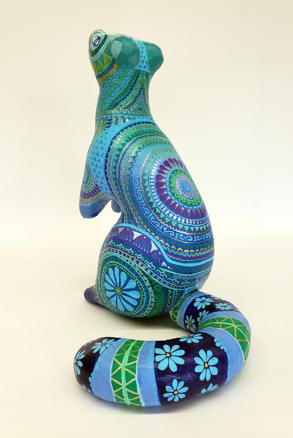 A colorful sculpture of a mongoose painted in mosaics of purples, greens and blues.